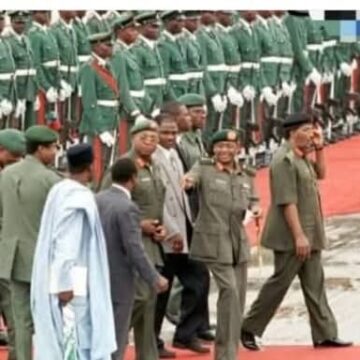 A historic photo from 1996 captures Head of State General Sani Abacha at the Abuja airport, surrounded by key figures in his administration. Behind him is his Chief Security Officer (CSO), Major Hamza Al-Mustapha, a man known for his fierce loyalty and controversial role during Abacha’s regime.